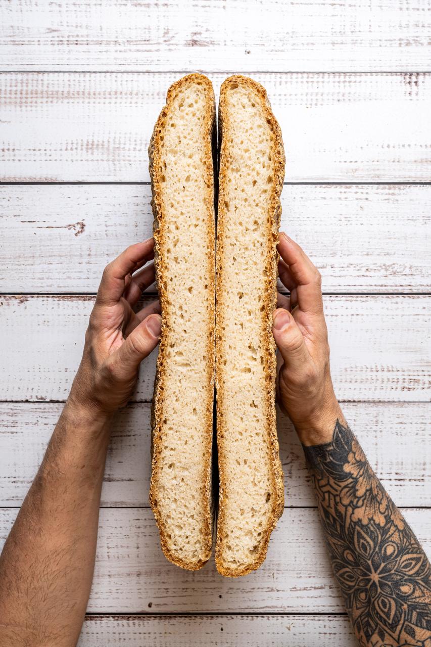 A long gluten-free loaf broken open by hand
