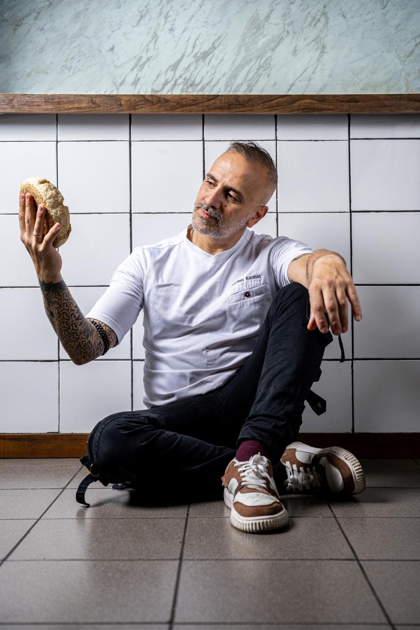 Chef Marinos Kosmas sitting on the bakery floor holding a fresh bake